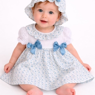 Bebé a usar vestido branco e azul com laços azuis e chapéu combinado