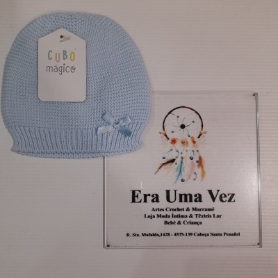 Gorro azul claro de malha com etiqueta e placa com texto e imagem ao lado.