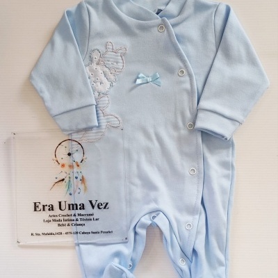 Macacão de bebé azul claro com bordado e laço azul e cartaz sobre superfície branca