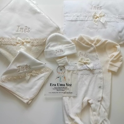 Conjunto de roupa de bebé branco bordado com nome Inês e laços.