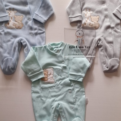 Três pijamas de bebé coloridos com bordados de animais, sobre fundo branco com placa transparente com texto
