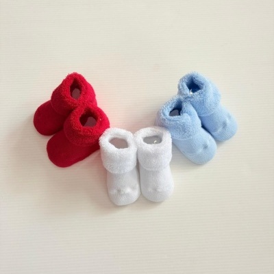 Três pares de meias para bebé em vermelho, branco e azul claro sobre superfície branca