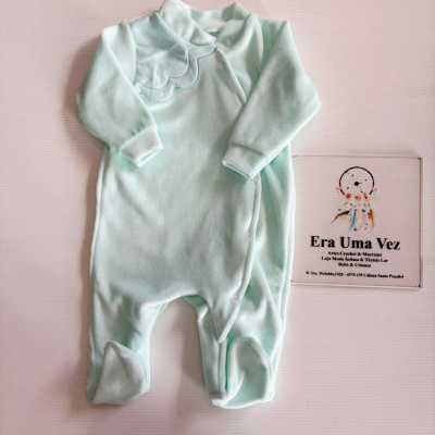 Pijama de bebé verde-pálido com botão de pressão e gola ondulada sobre superfície branca com placa de texto