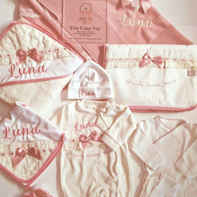 Conjunto de roupa e acessórios rosa e branco para bebé com detalhes de laços e bordados em rosa