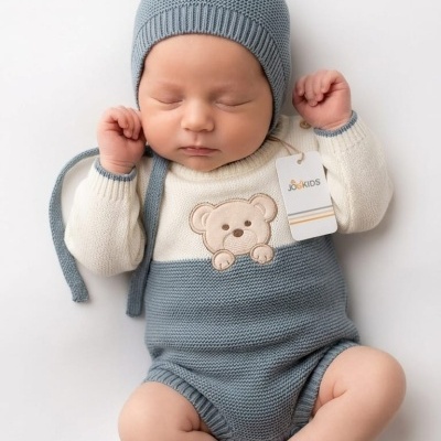 Bebé com fato de malha azul e branco com ursinho e chapéu azul