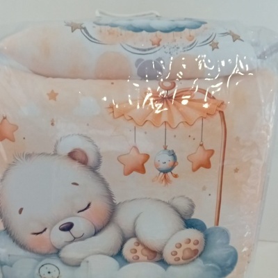 Ursinho branco dormindo sobre nuvens azuis com estrelas cor de laranja e móbile pendurado em embalagem plástica