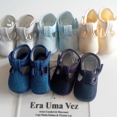 Cinco pares de sapatinhos para bebé em tecido multicoloridos com placa de informações da loja