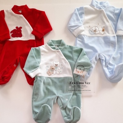 Três macacões de bebé em vermelho, azul claro e verde, com bordados e fechos de mola, sobre fundo claro.