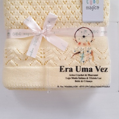Cobertor de malha amarelo claro com padrão rendado e etiqueta CUBO mágico