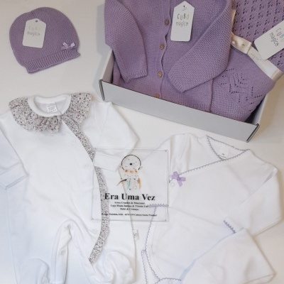 Conjunto de roupa de bebé com peças lilás e brancas organizadas sobre superfície branca