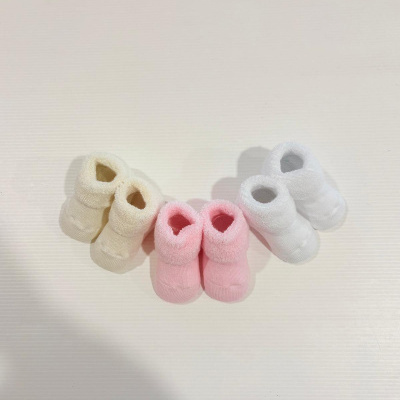 Três pares de meias de bebê em bege, rosa e branco sobre fundo branco.