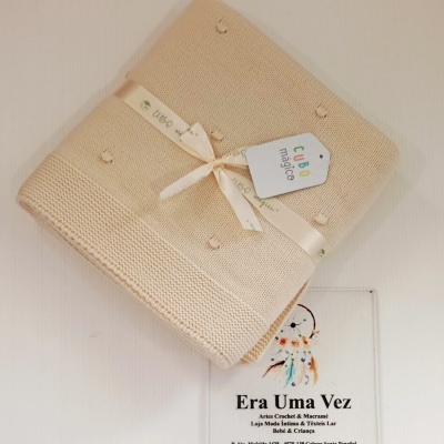 Manta bege com pompons e placa de loja na parede