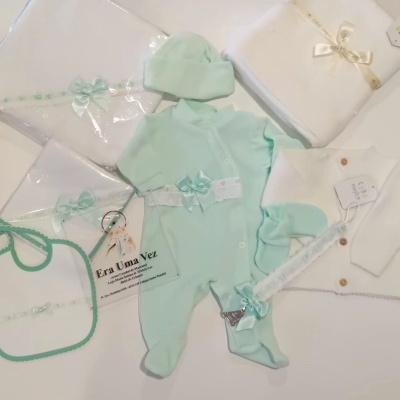 Conjunto de roupa de bebé verde claro e branca com acessórios e pacotes em cima de superfície clara