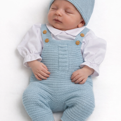 Bebé vestido com macacão azul claro e gorro correspondentes e camisa branca, deitado.