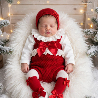 Bebé vestido com roupa vermelha e branca, deitado em fundo branco felpudo com decoração natalícia.