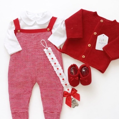 Conjunto de roupa de bebé com camisa branca, jardineiras vermelhas, casaco de malha vermelho, sapatinhos vermelhos e fita com laço.