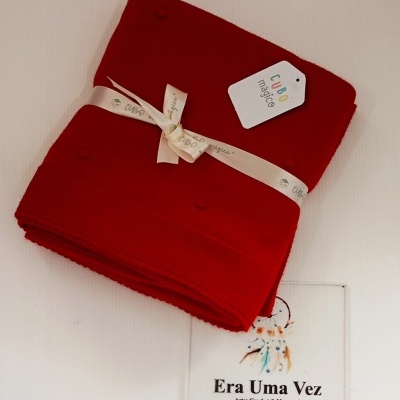 Manta tricotada vermelha com etiqueta e fita CUBO mágico sobre cartão promocional da loja