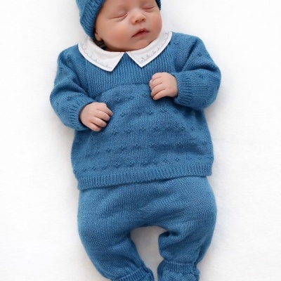 Bebé vestido com roupa de malha azul e gola branca, deitado sobre fundo branco.