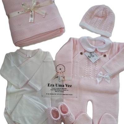 Conjunto de roupa de bebé rosa e branca com manta, macacão, gorro, body, calças e sapatinhos de malha.