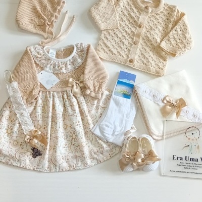 Conjunto de roupa de bebé creme e bege com vestido, cardigan, gorro, meias, sapatos e manta