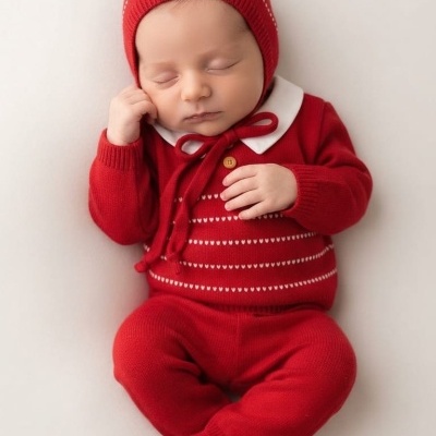 Bebé a dormir vestido com conjunto vermelho de malha, incluindo camisola com gola, calças e gorro.