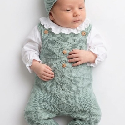Bebé com macacão e gorro de tricô verde claro deitado sobre fundo branco