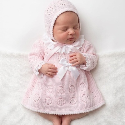 Bebé com vestido e gorro de malha rosa claro com detalhes brancos