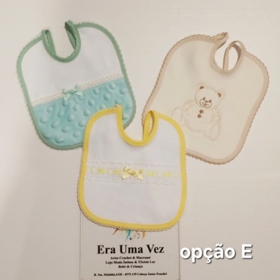 Três babetes de bebé em várias cores e texturas sobre superfície branca