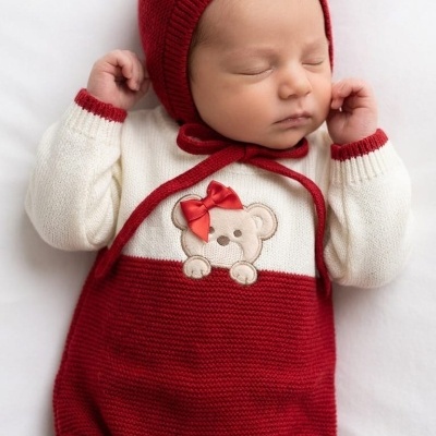Bebé recém-nascido com macacão de malha vermelho e branco com ursinho e gorro vermelho a dormir
