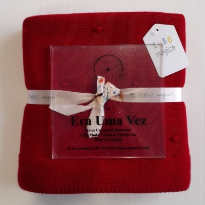 Manta vermelha com relevo de nós, embalagem transparente e etiquetas CUBO mágico e Era Uma Vez.