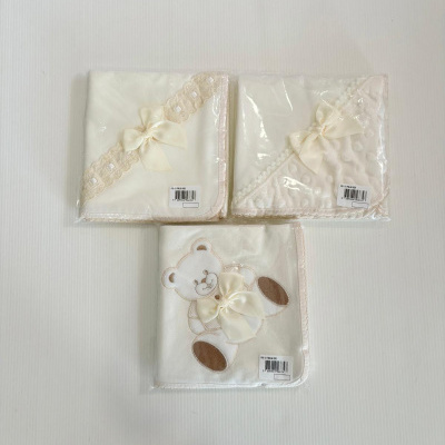 Três mantas de bebé creme com laços e urso bordado embaladas em plástico.