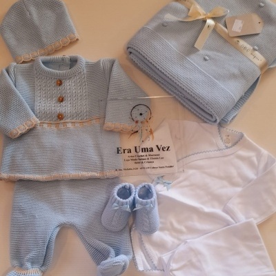 Conjunto de roupa de bebé azul claro com body branco e manta dobrada com fita.