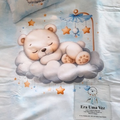 Conjunto de cama azul com estampa de urso bebé a dormir numa nuvem e estrelas e etiqueta Era Uma Vez