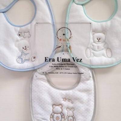 Três babetes de tecido branco com bordas coloridas e bordados de ursinhos, com texto promocional no centro.
