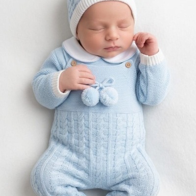 Bebé com macacão e gorro azul claro em malha com padrão de tranças