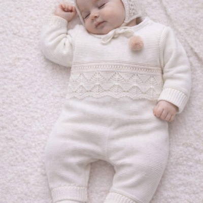Bebé dormindo com macacão de malha branco e chapéu de malha com pompom cor de rosa