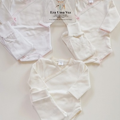 Conjuntos de roupa de bebé com bodies de manga longa e calças em algodão branco e bege com detalhes em croché, com placa informativa no centro