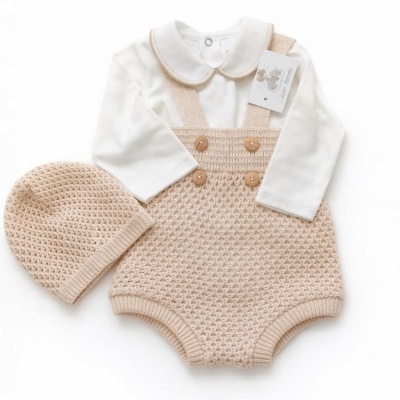 Conjunto de roupa de bebê com body branco, jardineira bege de malha e gorro bege.