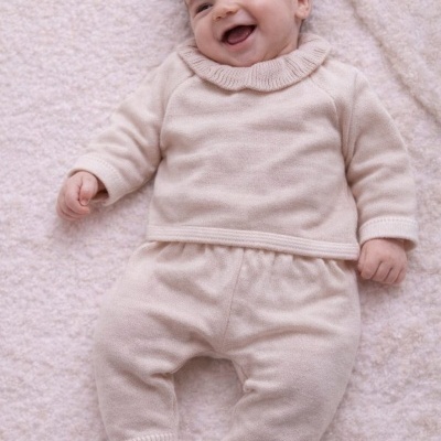 Bebé sorridente com roupa de malha bege claro sobre superfície branca felpuda