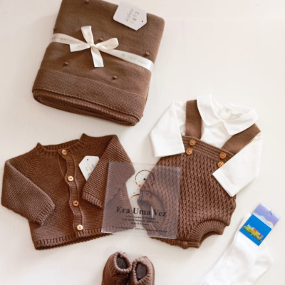 Conjunto de roupa de bebé castanho e branco em tecido de malha, com manta e sapatinhos.