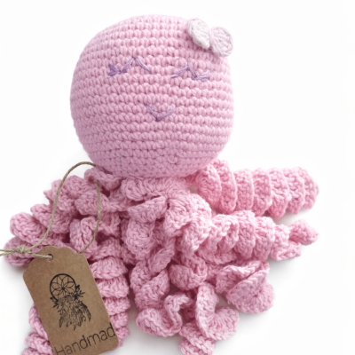 Brinquedo de pulpo rosa feito de crochet com olhos bordados e laço branco