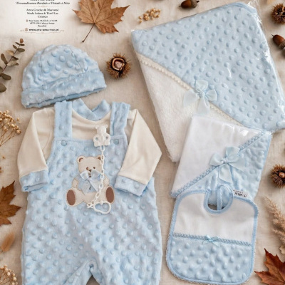Conjunto de roupas de bebé azul claro com acessórios sobre fundo bege com folhas e frutos secos.