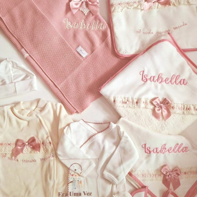 Conjunto de roupa e acessórios para bebé rosa e branco com bordados e laços.