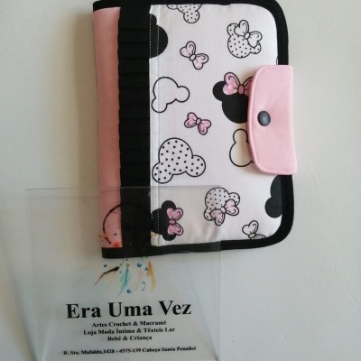 Capa de tecido branco com padrão de cabeças de rato e laços rosa e botão de pressão rosa junto a uma placa transparente com texto