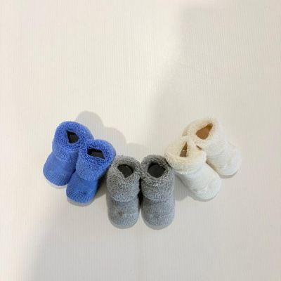 Três pares de meias de bebé felpudas em azul, cinzento e branco em superfície branca