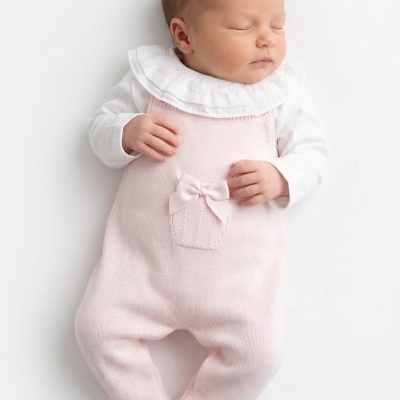 Bebé a dormir com roupa de malha rosa clara e camiseta branca sobre fundo branco.