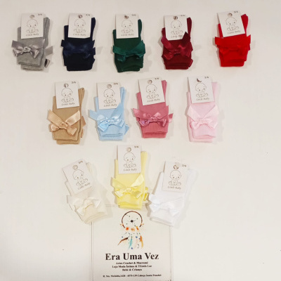 Meias para bebé em várias cores com laços e etiquetas, cartão com texto de loja em fundo branco.