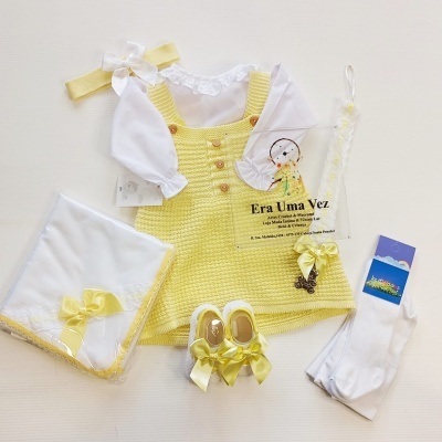 Conjunto de roupa de bebé amarelo e branca com vestido, camisa, sapatinhos, meias, faixa e manta
