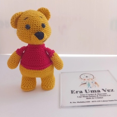 Ursinho de croché amarelo com colete vermelho e cartão de visita