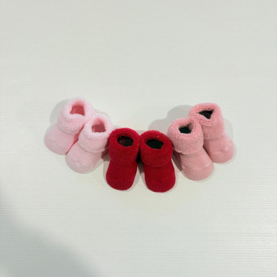 Três pares de meias botins de lã para bebé em rosa claro, vermelho e rosa escuro, sobre fundo branco.